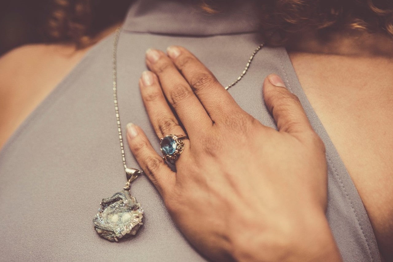 Woman with hand across her geode necklace wearing an antique aquamarine ring