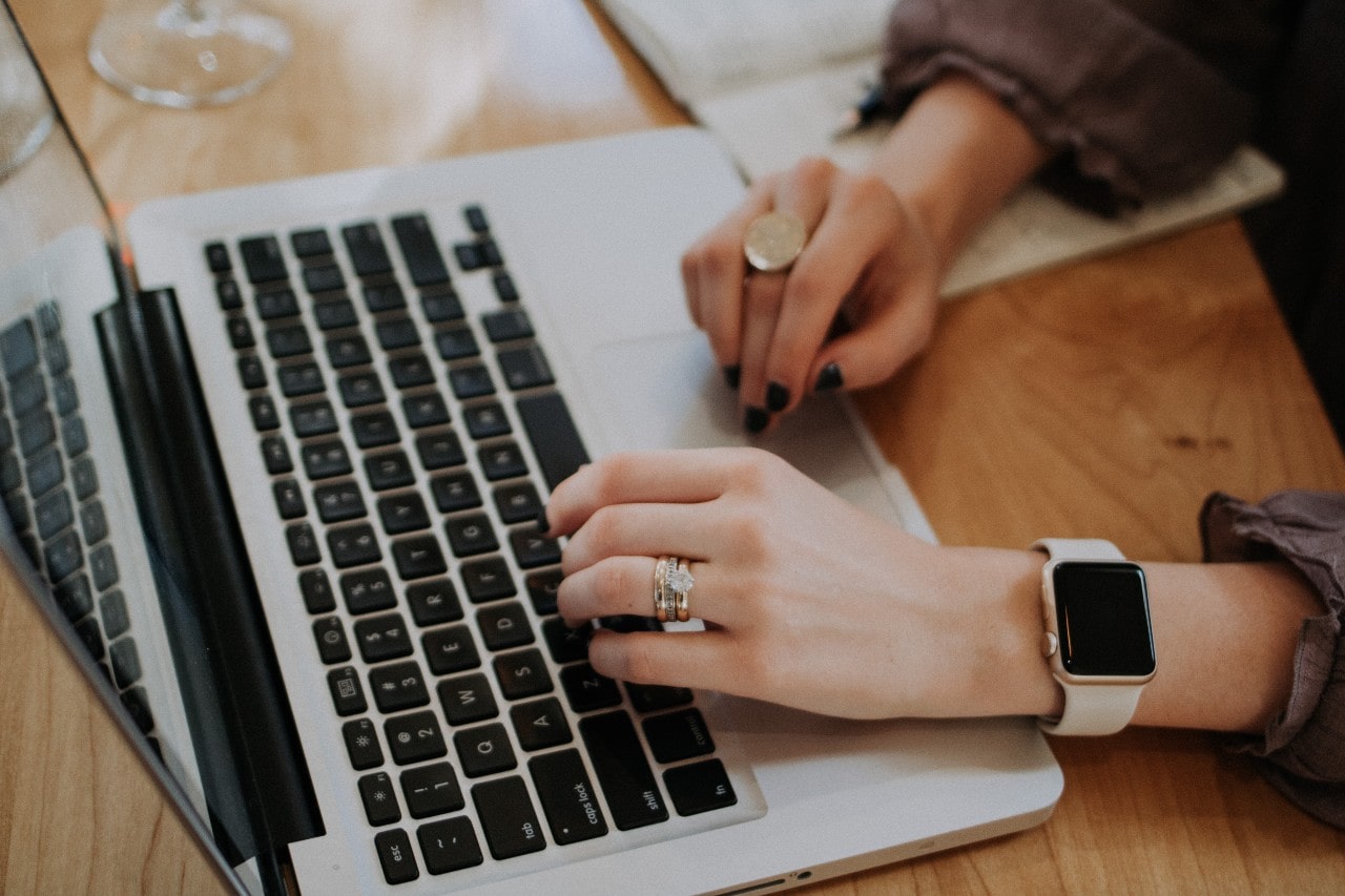 A woman wearing a diamond wedding ring set while typing on a laptop, with a smartwatch on her wrist. A woman wearing a diamond wedding ring set while typing on a laptop, with a smartwatch on her wrist.