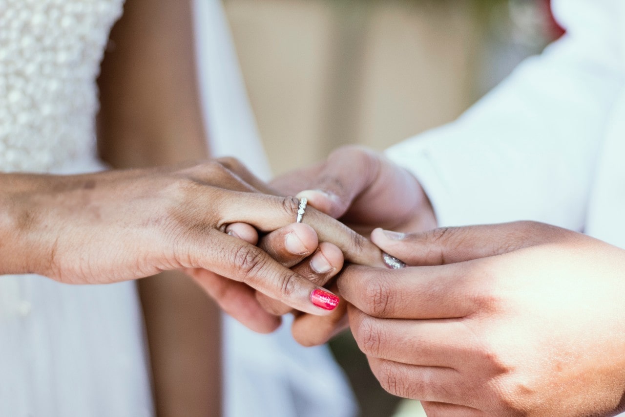 A close-up of a groom placing a sparkling white gold wedding band on the bride's finger during their wedding ceremony. A close-up of a groom placing a sparkling white gold wedding band on the bride's finger during their wedding ceremony.