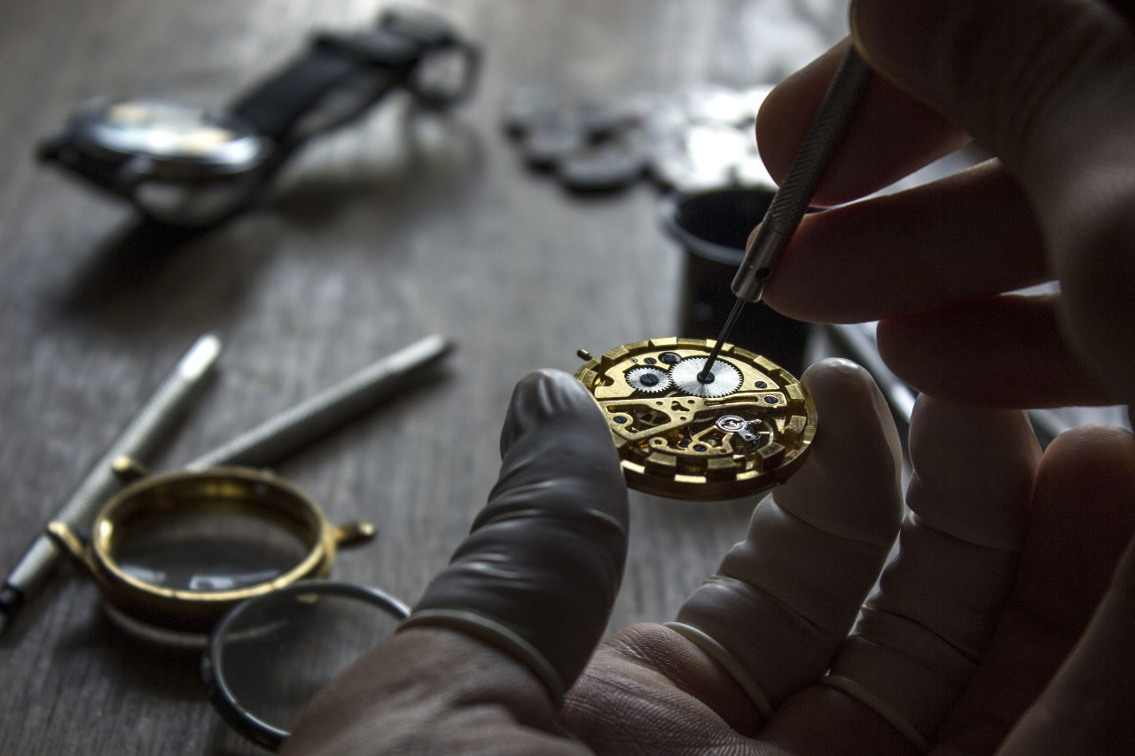 A horologist wearing finger covers repairs the inner mechanisms of a watch