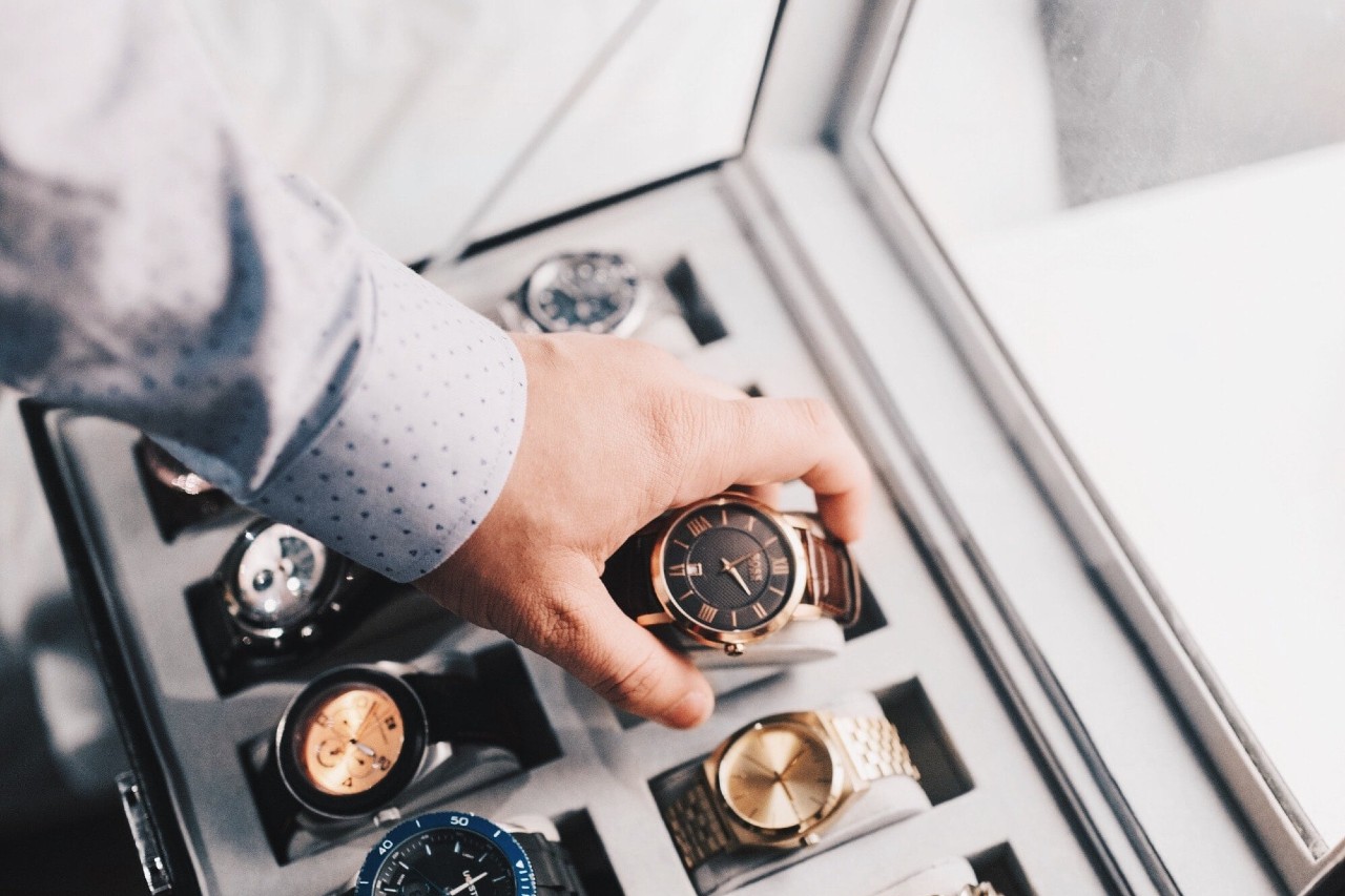 A man wearing a button down shirt selects a vintage-style timepiece from his watch collection as he gets ready