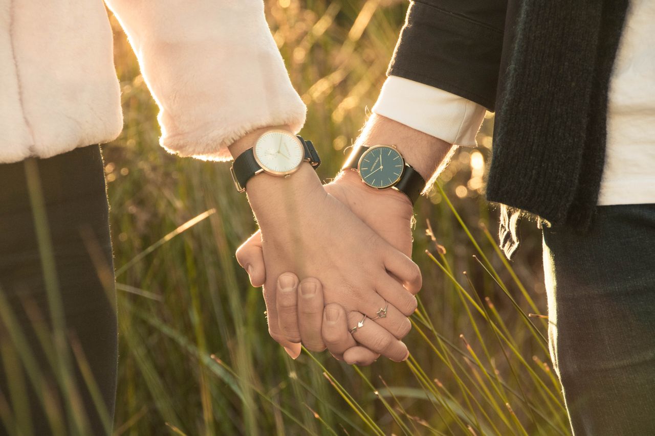A couple holding hands wearing matching watches, except one has a white dial and the other has a black dial