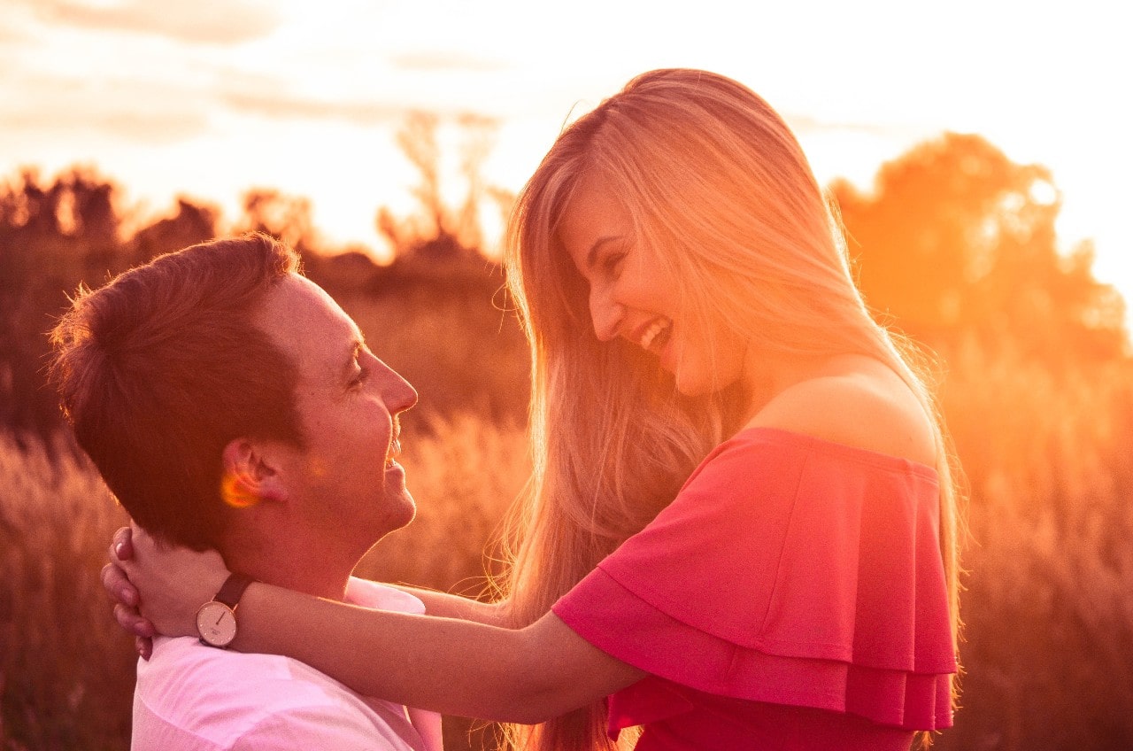 A man and woman smiling at each other in a field at sunset