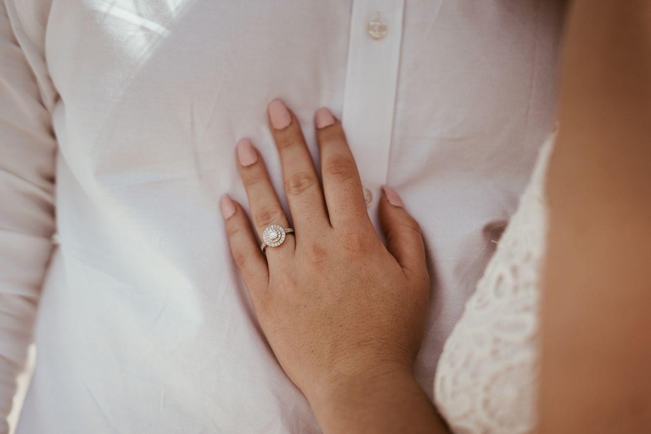 A close-up of a bride-to-be resting her hand on her groom’s chest, an ornate engagement ring on her finger.