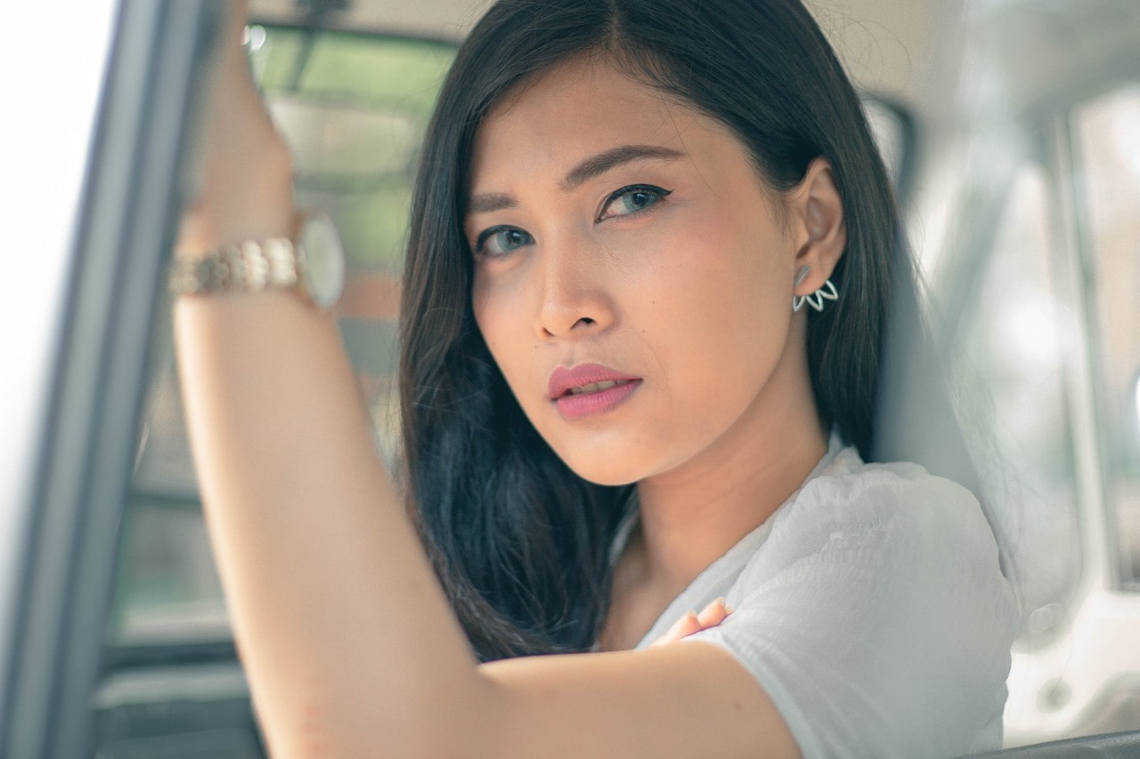 a woman sits in a van, wearing casual jewelry and clothing.