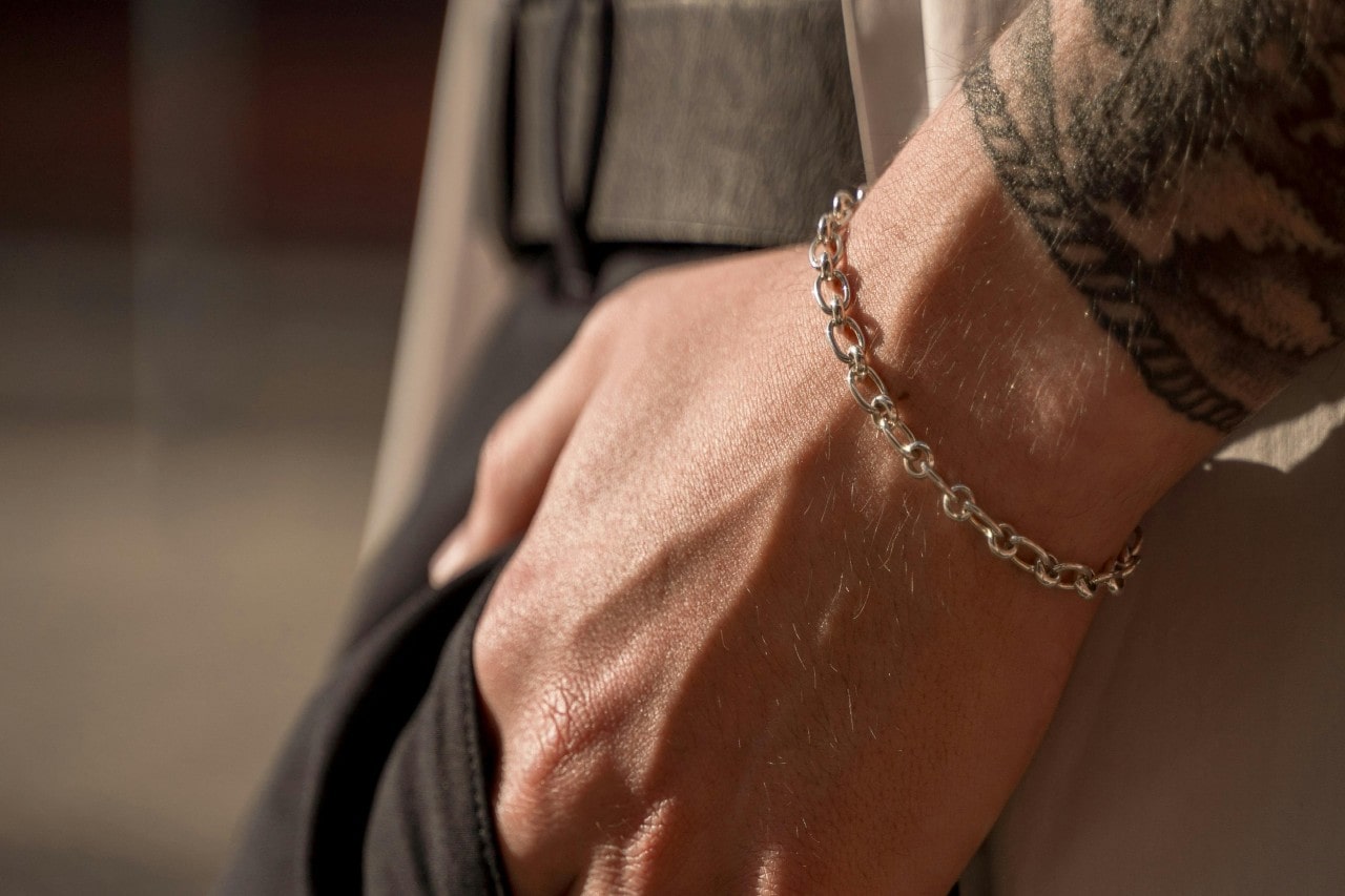 A man’s hand in his trouser pocket, a silver chain bracelet on his wrist.