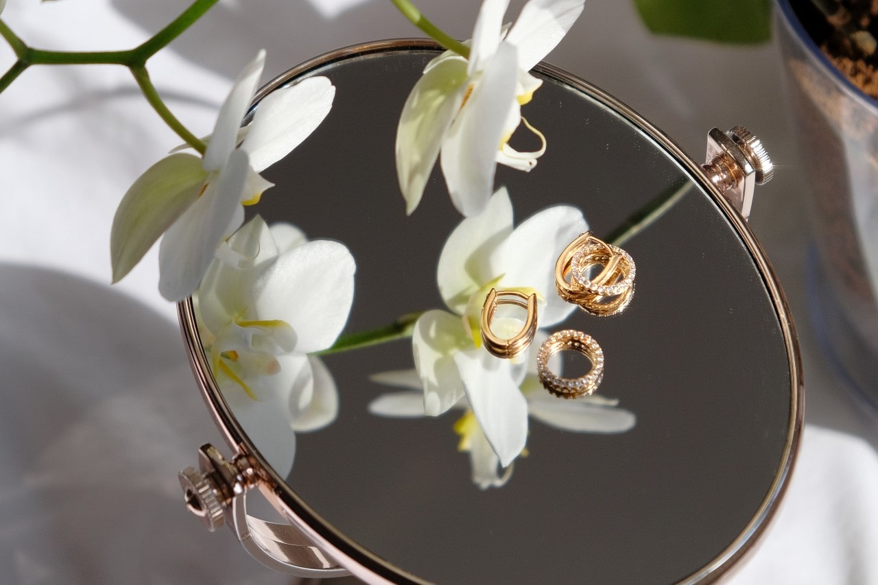 Gold jewelry atop a vanity mirror surrounded by orchids.