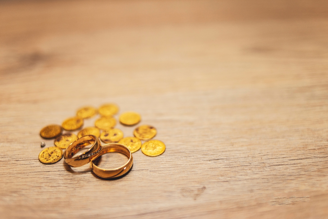 A close-up of two gold rings and a handful of gold coins on a wooden tabletop.