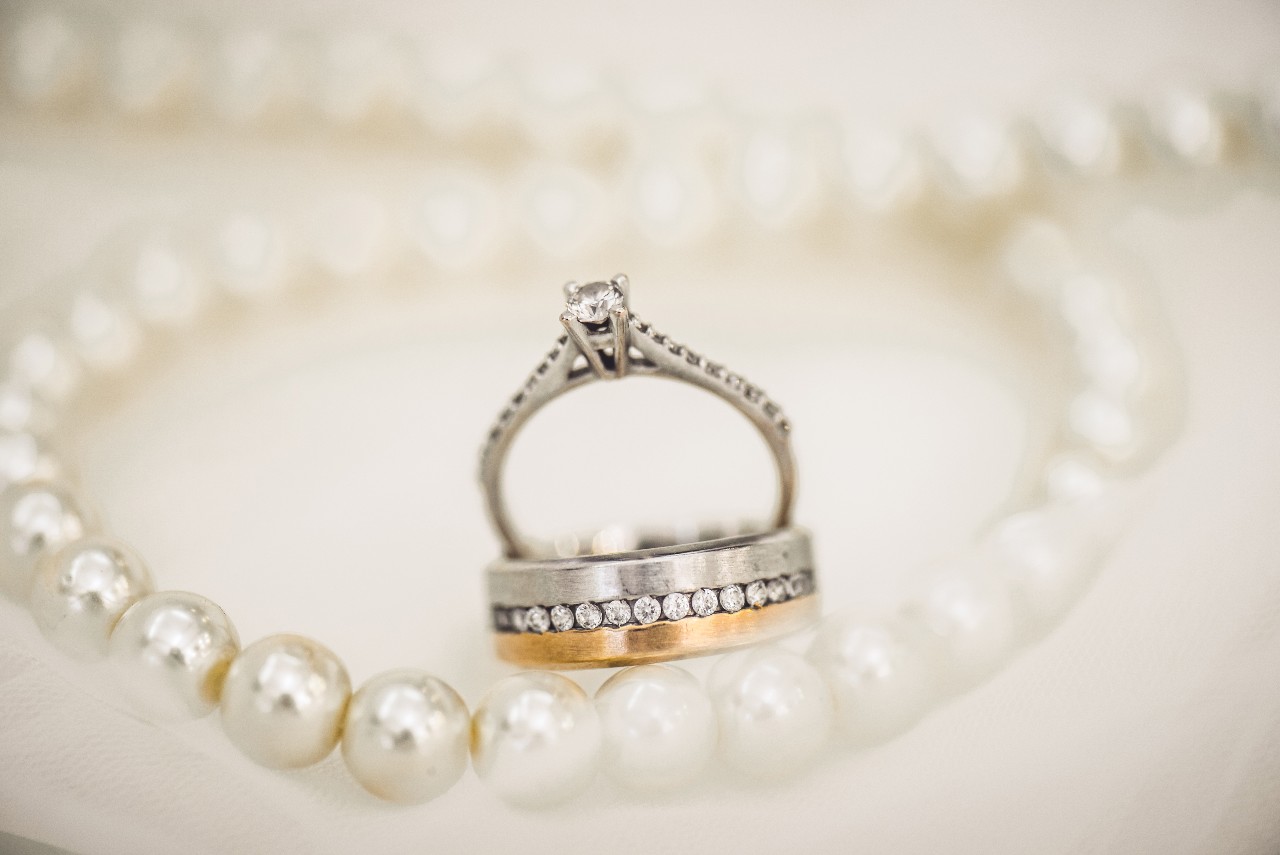 a side stone ring and two-tone men’s wedding band sit among a pearl necklace.