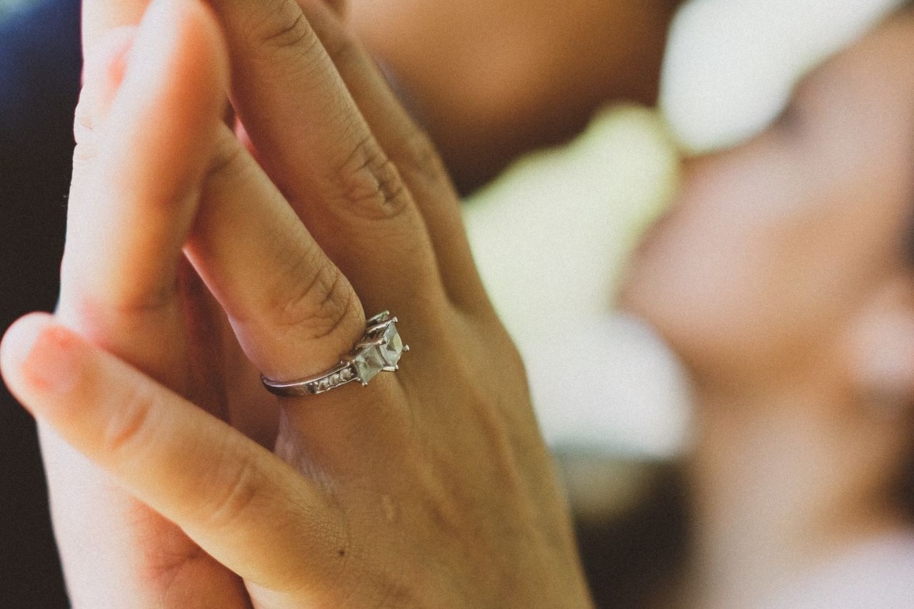 A woman with a three-stone side stone engagement ring touches hands with a man.