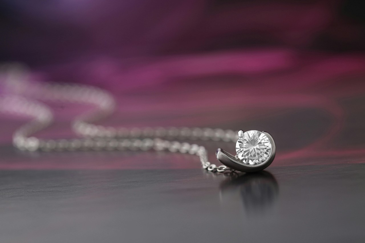 close up image of a white gold pendant necklace featuring a round cut diamond