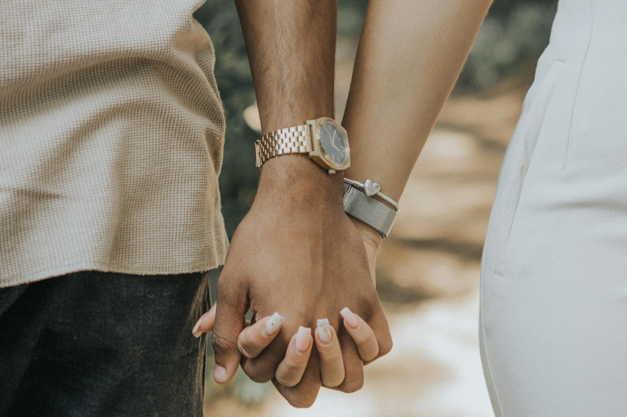 a man and woman holding hands–the man wearing a yellow gold watch