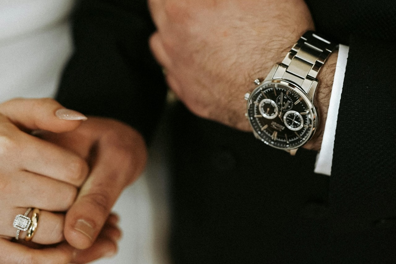 a bride and groom holding hands–the groom wearing a black and silver watch