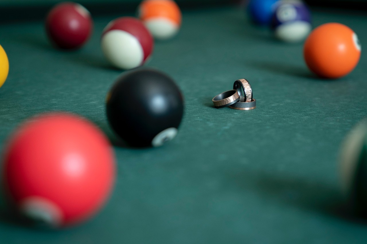 Three men’s wedding bands displayed on a pool table.