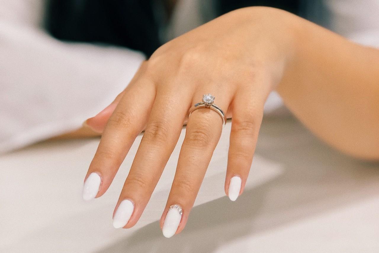 A close-up of a woman’s manicured hand, a platinum engagement ring on her finger.