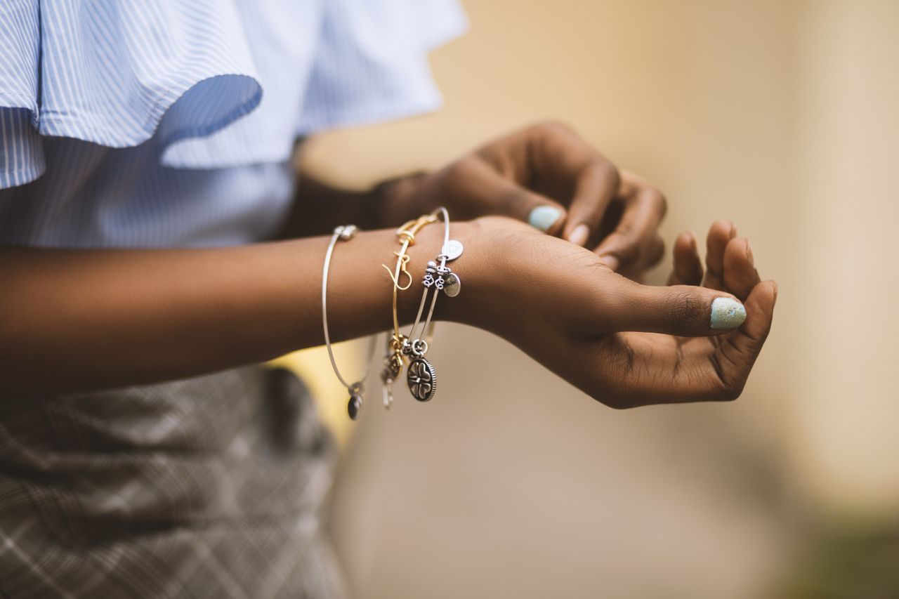 A close-up of a young woman’s wrists adorned with fashionable stacked bracelets made of different precious metals.